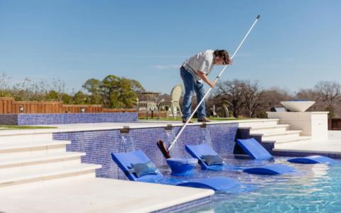 Pool cleaning and maintenance worker cleaning tile on side of pool.